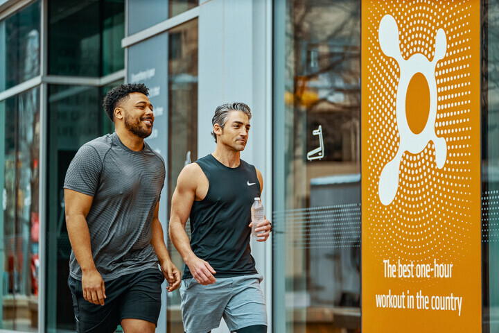 Two men walking outside of a fitness studio, with orange branding for Orange Theory Gym