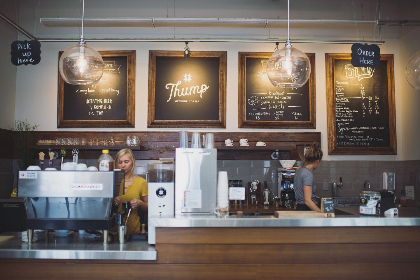 An landscape view of a coffee checkout counter, moody lighting and dark menu boards, specialty coffee equipment lines the counters.