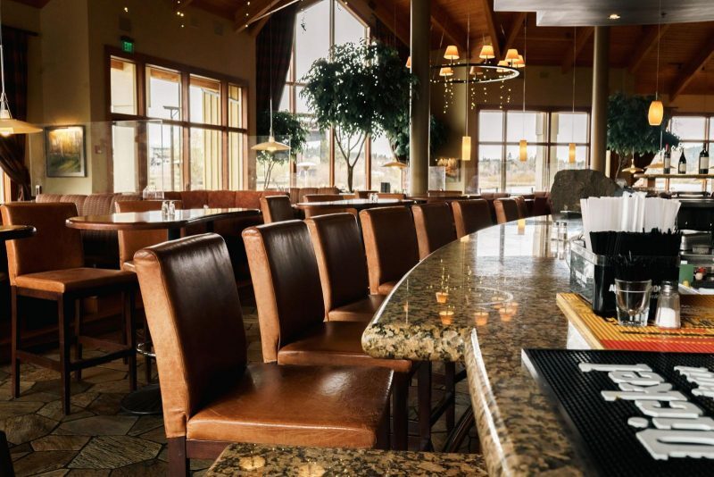 A bar seating area in a restaurant with moody lighting and greenery.