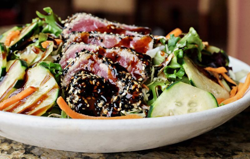 A white plate full of salad and various other veggies topped with a seasoning.