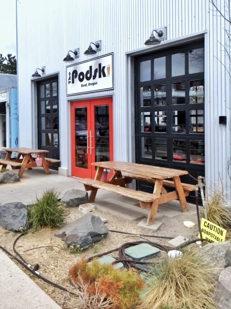 A white building with a red door, a picnic table out front and big black garage doors with windows.