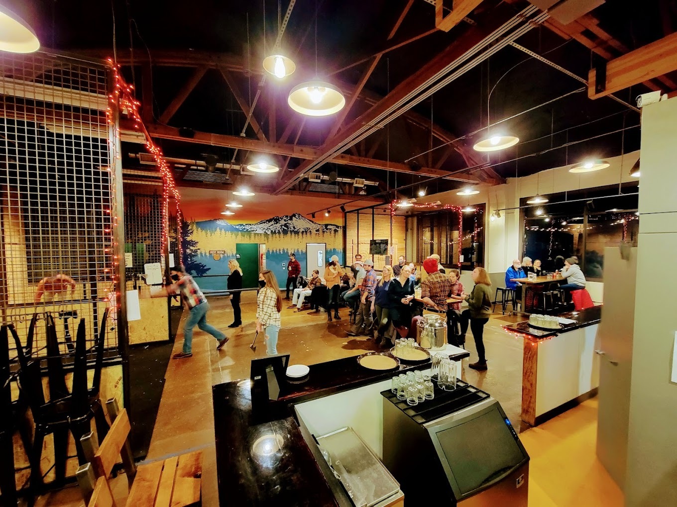 Inside look of an ax throwing restaurant, a view from behind and aside the counter, shows off seating and ax throwing lanes.