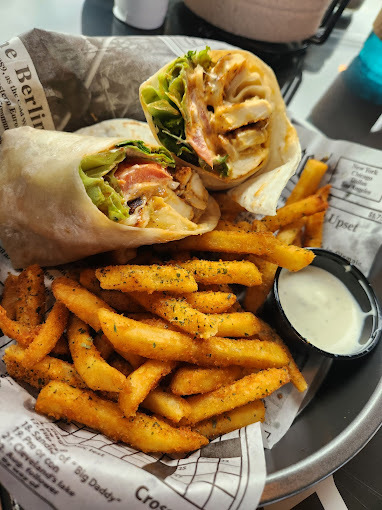 Two burritos, fries, and a cup of sauce, on top of paper in a bowl.
