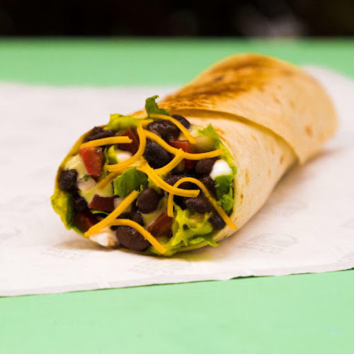 Burrito wrap made with olives, cheese, guacamole, and lettuce. It is set on a light colored Taco Bell napkin.