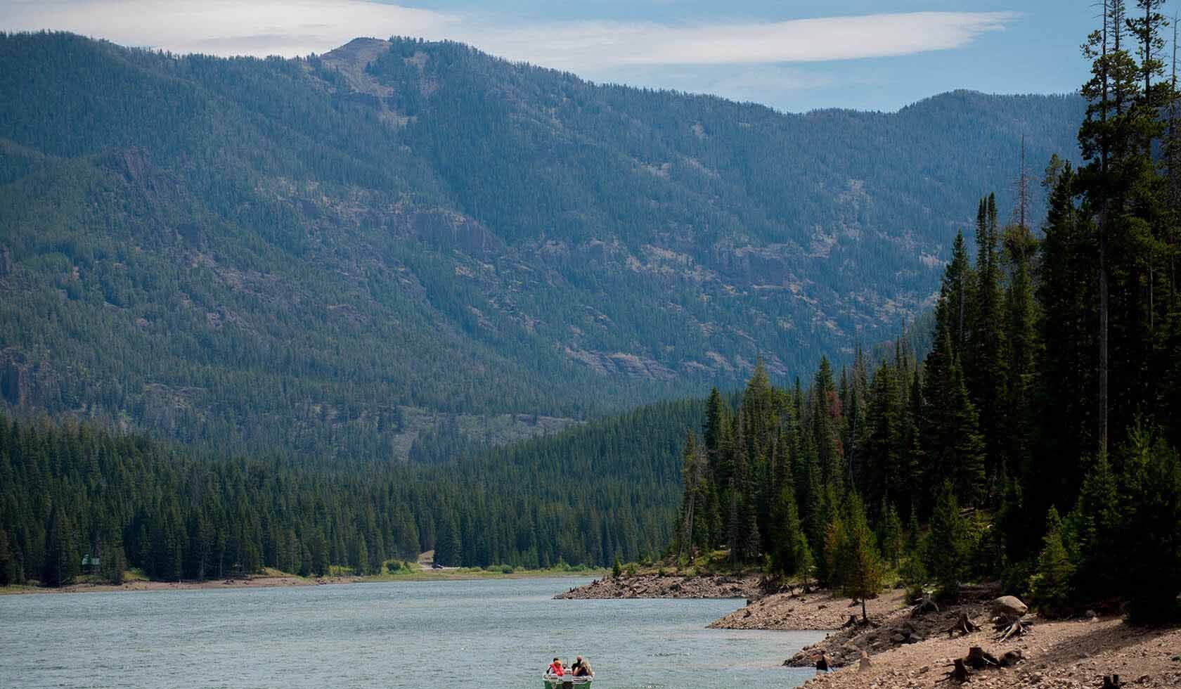 View of high mountains and numerous trees. A lake is seen in the foreground of the image.