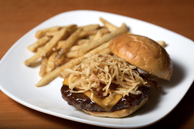 Burger with sauce and cheese and a side of fries, all on a white square plate.