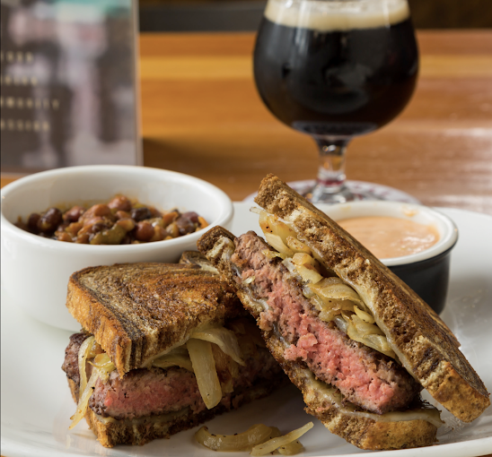Sandwich slices with hamburger patties, a bowl of soup, a cup of sauce, and a glass of wine.