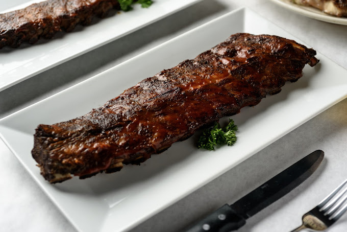 Rack of ribs centered over a small piece of broccoli, all on a white rectangular plate.
