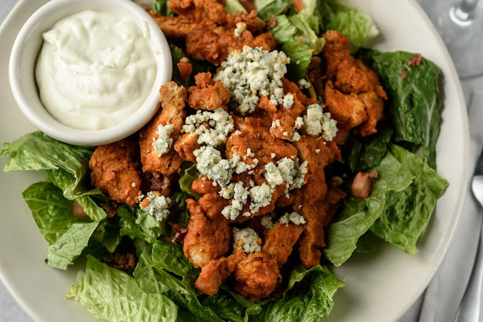 Breaded chicken and salad greens with a side of white sauce in a cup.