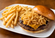 Cheeseburger topped with crispy fried onion strings and served with a side of golden French fries on a white plate.