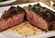 Thick grilled steak sliced into two portions, featuring a charred crust and medium-rare center on a white plate with a light herb garnish.