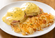 Eggs Benedict topped with hollandaise sauce and herbs, served alongside crispy golden hash browns on a white plate.