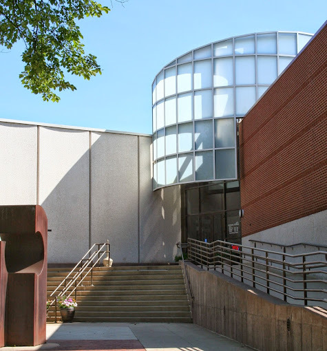 An outdoor view of an entrance to a building, a large building with a large glass covered entry area.