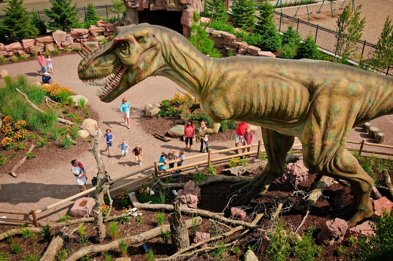 An areial view of an outdoor area of a museum, a large t-rex dinosaur fenced in is featured in this picture.