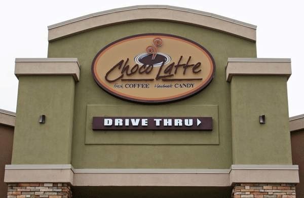 An outdoor view of a cafe's sign above their entrance. A yellow sign with red cursive lettering that reads Choco Latte and a small black sign that reads drive thru below the larger yellow sign.
