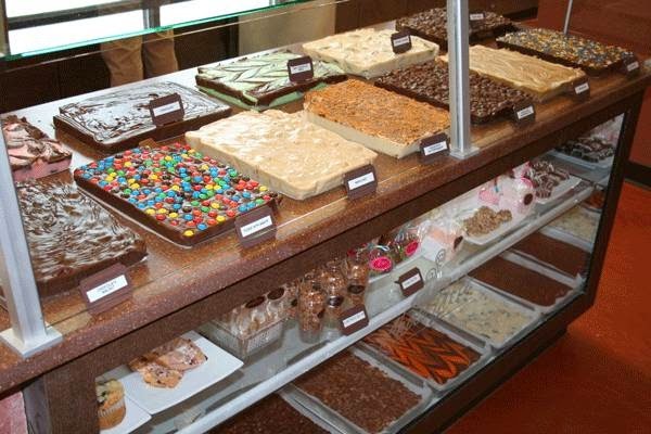 A view of a sweets display case filled with trays of fudge, muffins, parfaits, and cookies.