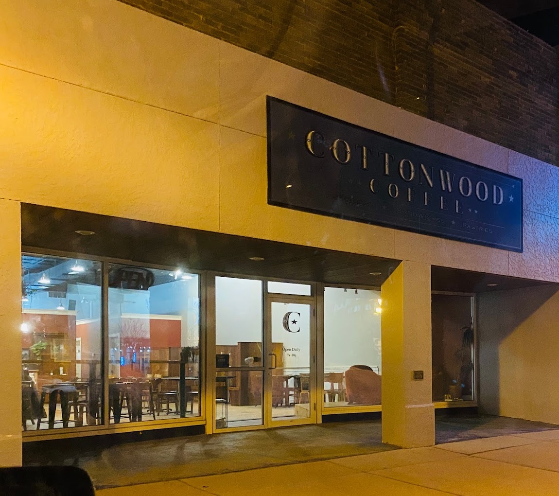 An outdoor view of an restaurant in a large beige building with large windows out front.