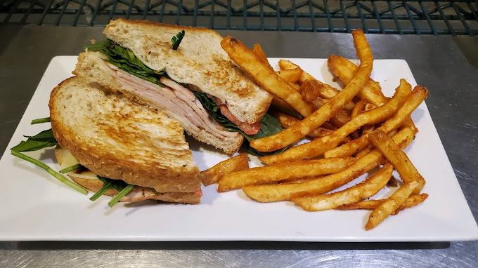 A white plate consisting of a sandwich cut in half and served with a side of sweet potato fries.