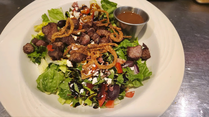 A white plate consisting of a salad topped with feta, steak and onions.