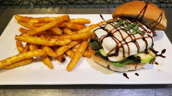 A white plate with an open burger, topped with cheese and a balsamic glaze, served with a side of sweet potato fries.