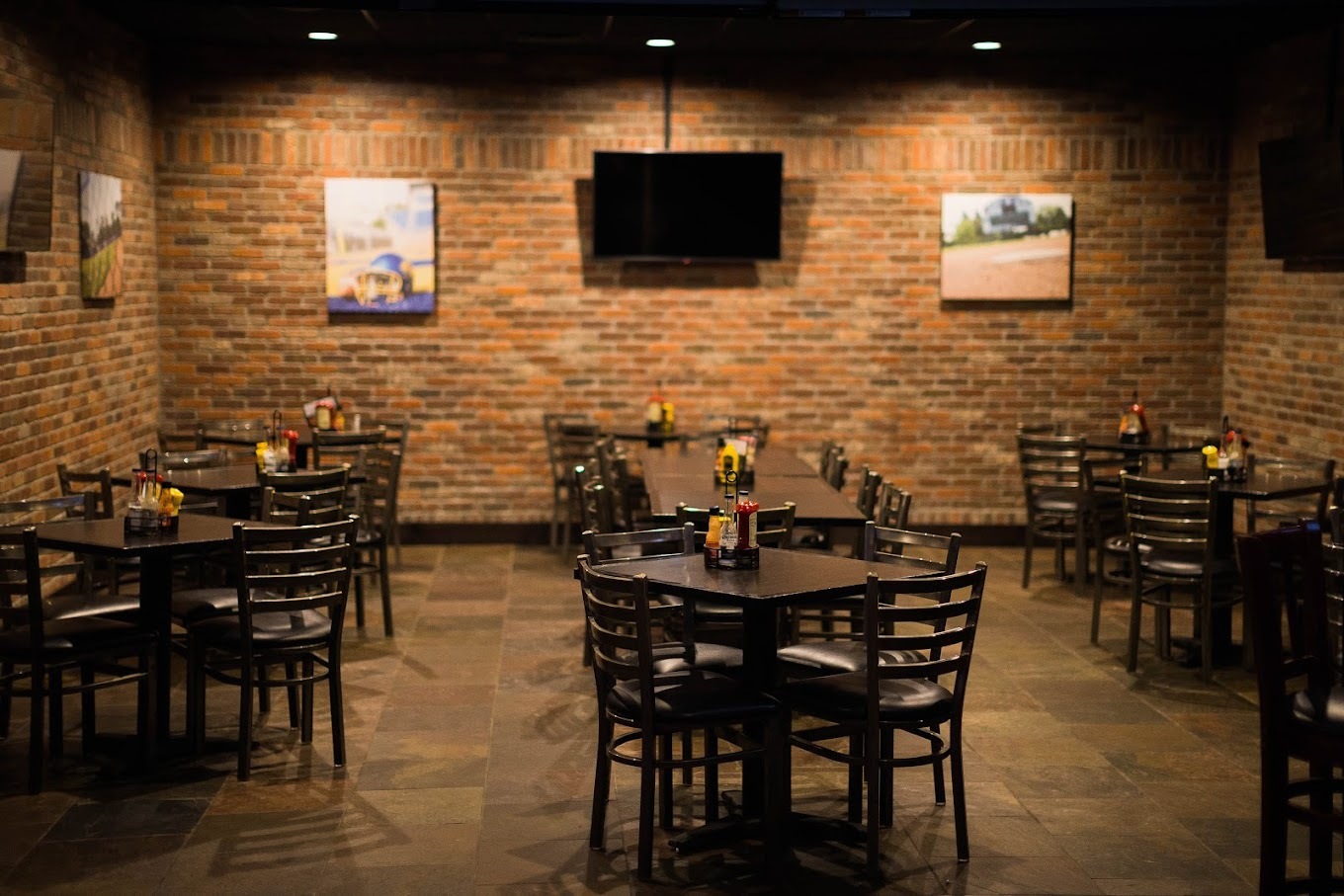 A view of a seating area in a pub, brick walls, dimly lit, and posters on the walls. Plenty of tables and chairs fill the room.