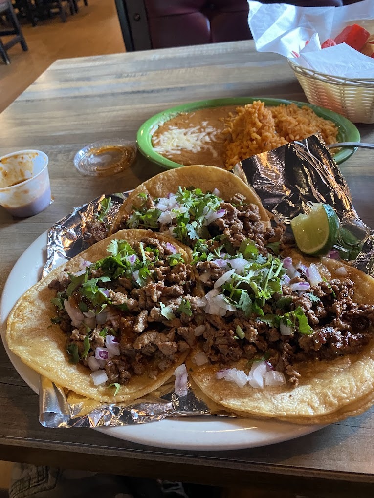 A white plate filled with three tacos and a side of rice and beans.