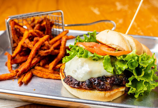A rectangular metal plate with a lettuce, sauce, and meat burger and crispy fries falling out of a metal cross hatched container.