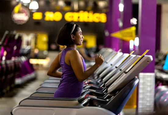 Woman in a purple tank top running on a treadmill.