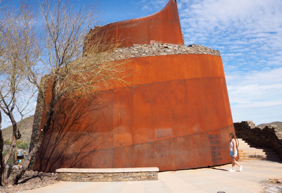 Spiral orange building with a leafless tree on the left side. A girl is walking on the right side.
