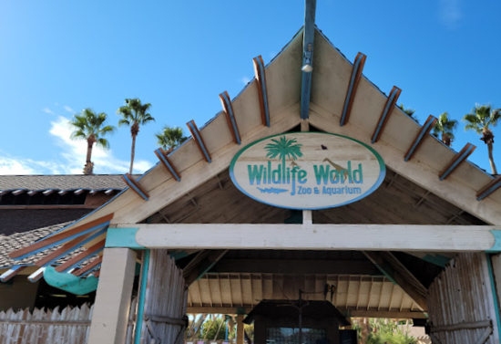 Upward view of a brown, beige, and blue building entrance. The circular sign above the entrance says "Wildlife World Zoo and Aquarium."