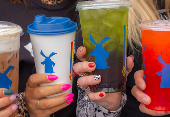 Close view of four manicured hands holding four different Dutch brothers drinks. Three are iced drinks and one is a hot drink.