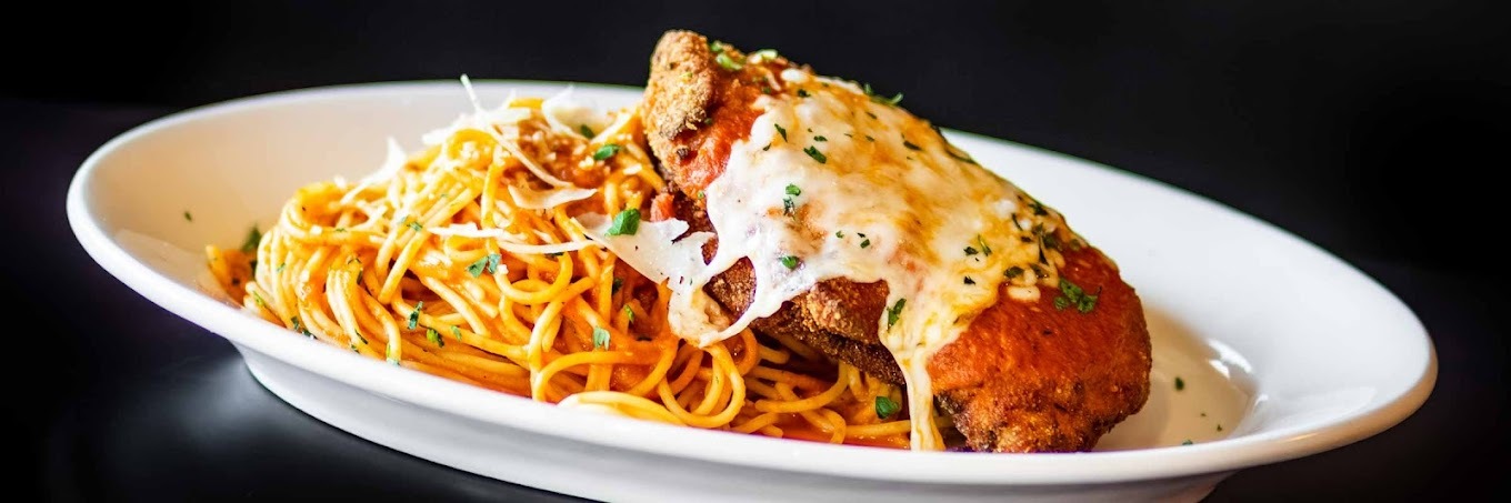 A white plate with pasta and chicken with red sauce and topped with cheese.