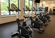 Modern fitness room with rows of stationary exercise bikes positioned near large windows filled with natural light.