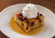 Warm bread pudding topped with whipped cream and served in a pool of buttery caramel sauce on a white bowl-shaped plate.