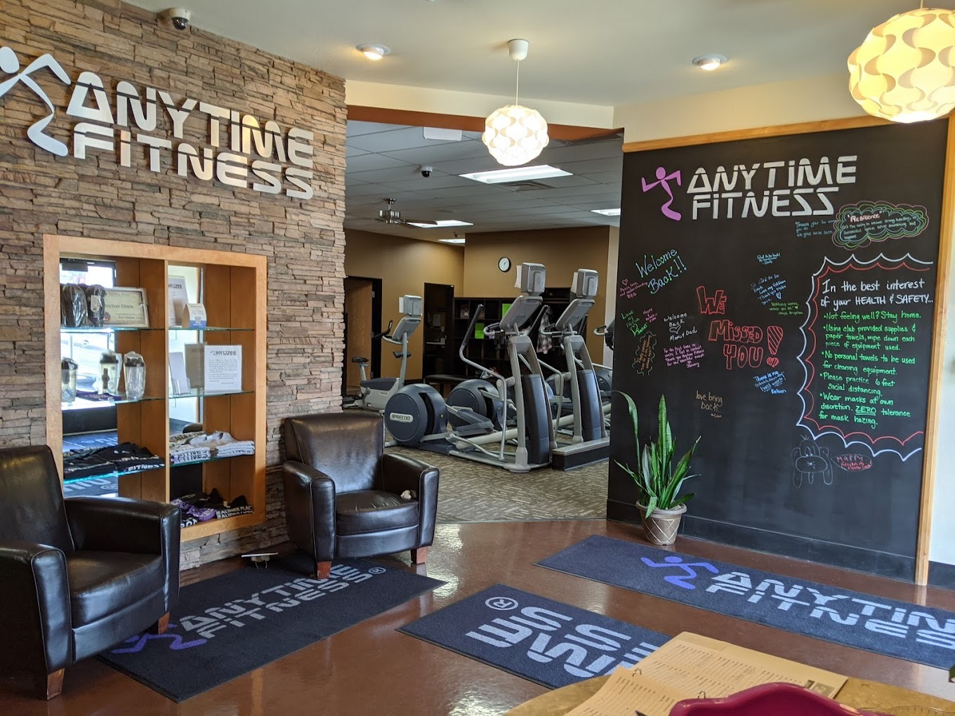 Anytime Fitness lobby with a set of black recliners, and a large chalkboard, a sign in silver reads Anytime Fitness