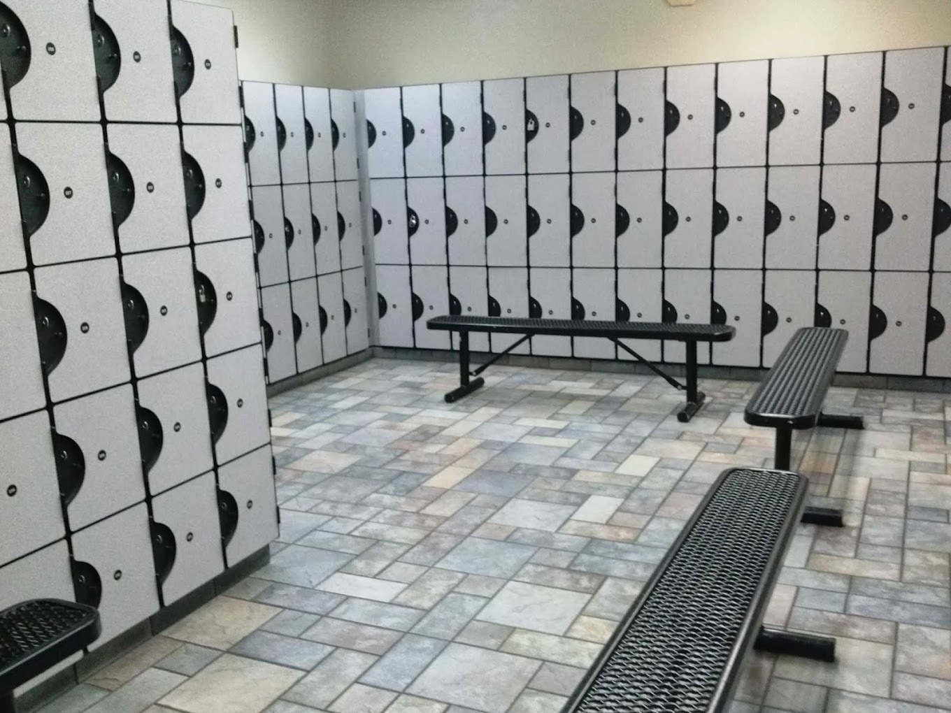 A room with tile flooring and benches lined with lockers on the walls.