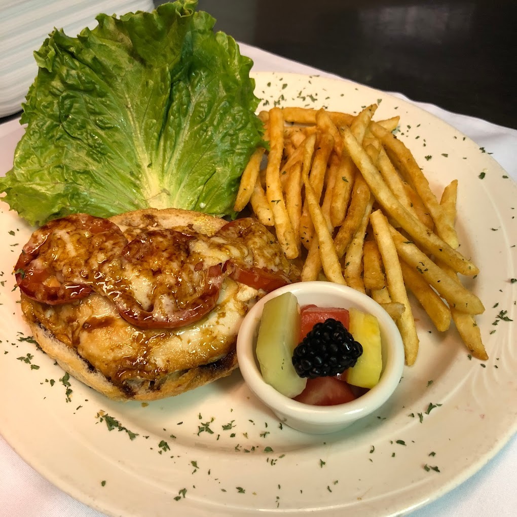 A white plate with a sandwich topped with cheese and tomato and a side of fries and fruit.