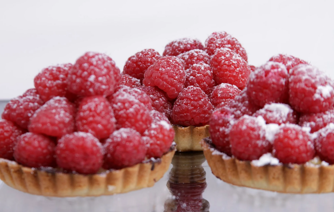 A set of three tarts full to the brim with raspberries and sprinkled powdered sugar.