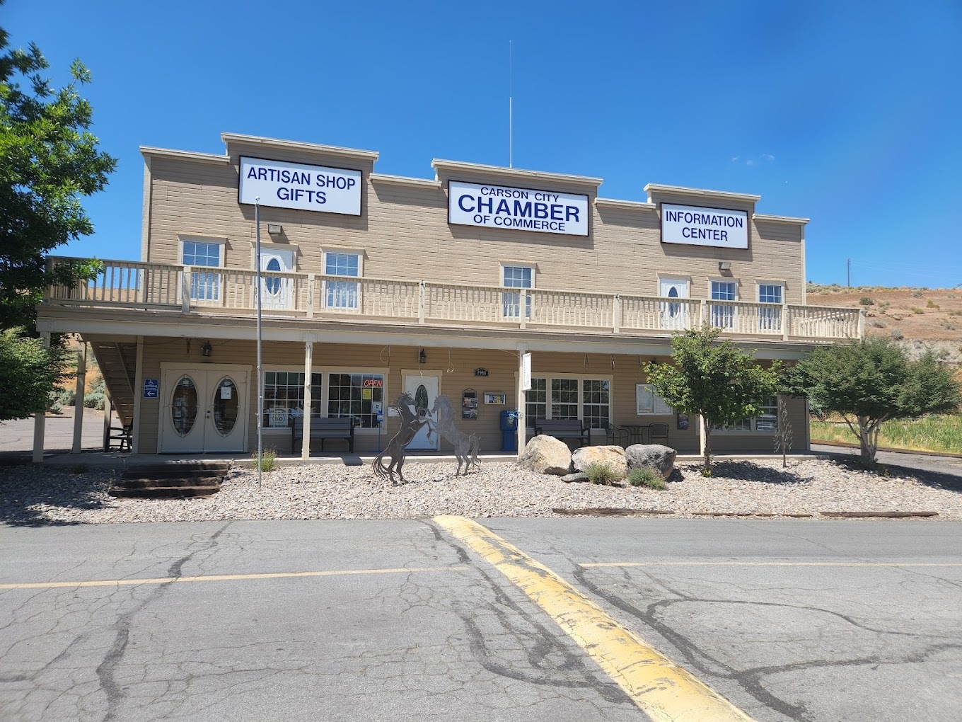 A saloon style type building in creme with an awning, above the awning there are signs directing to the Visitors Information Center.