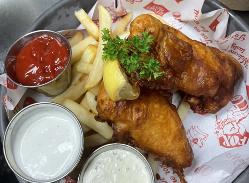 A view of a basket of fish and chips with three different sides of sauce.