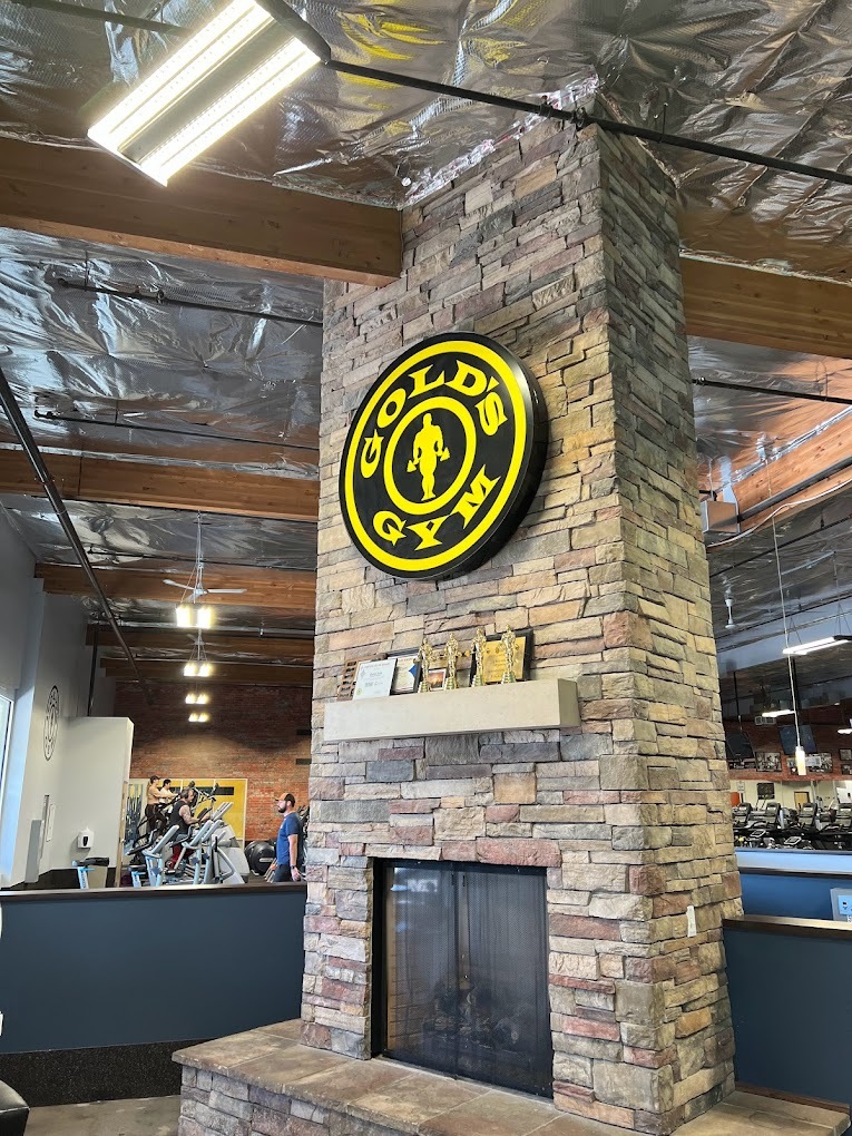 An inside view of a gym lounge area, with a fireplace and a black circular sign with yellow lettering.