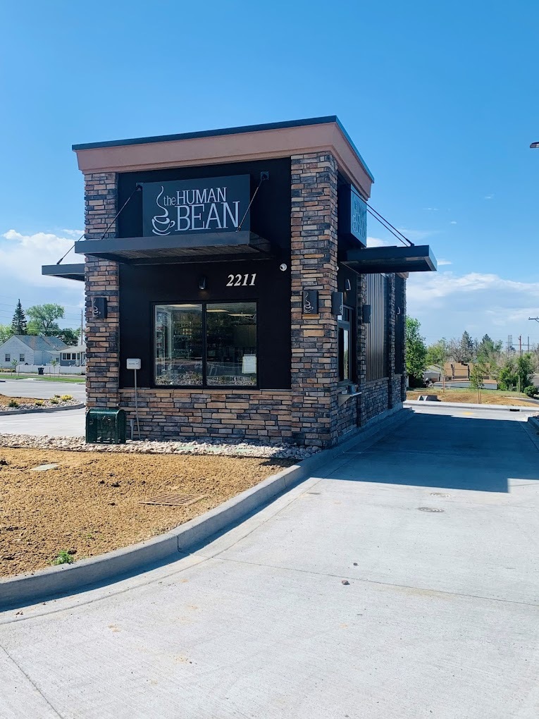 An outdoor view of a small drive-thru coffeehouse a modern styled building with a black sign out front reading "The Human Bean"