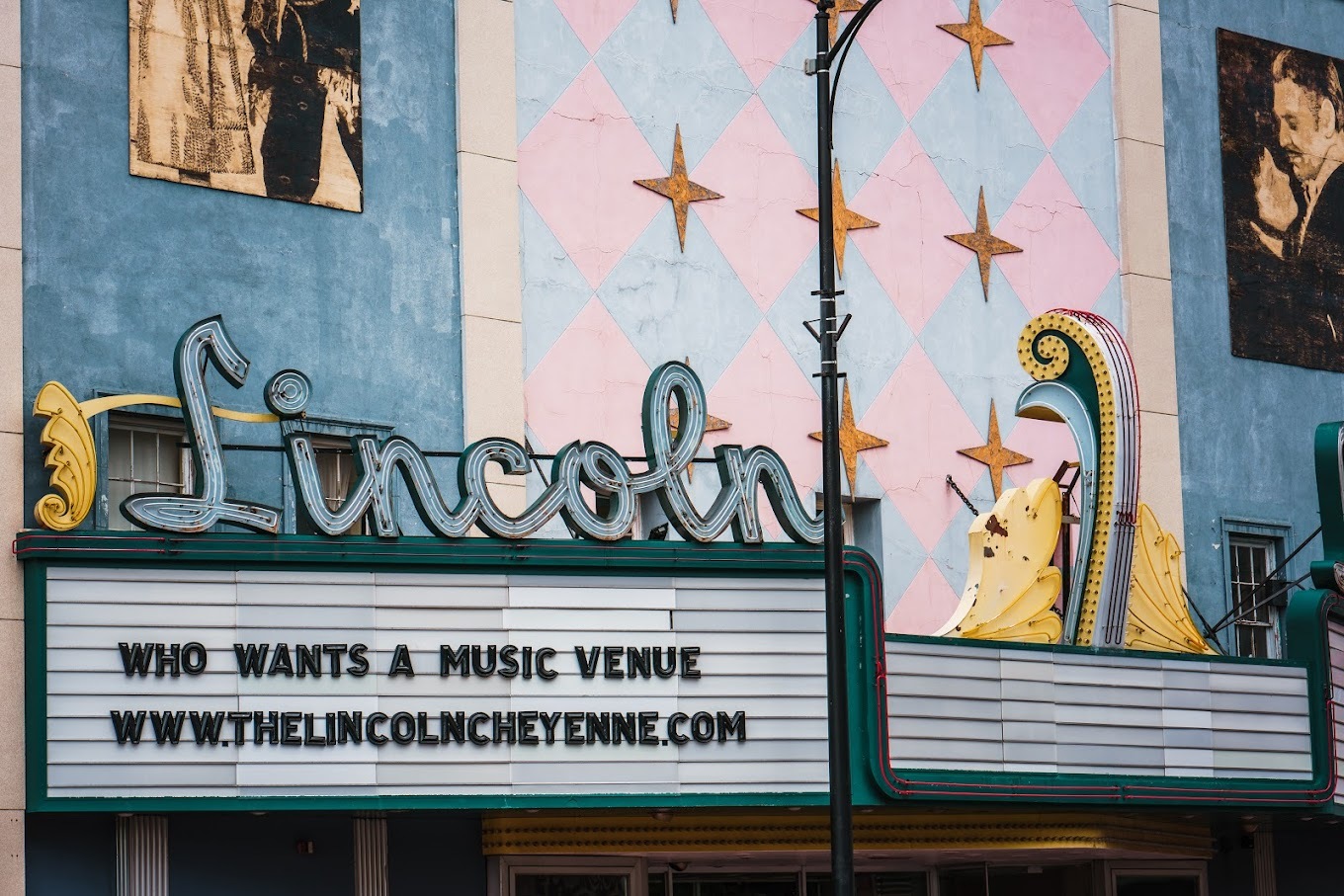 An outside view of a vintage theatre with decorative diamond print out front with white and pink, and a large marquee sign with the lettering 'Lincoln" above the marquee.
