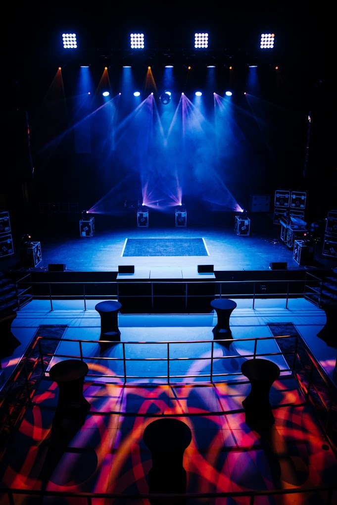 A view of a stage that is lit up, with a crowd of people surrounding the stage and cat walk.