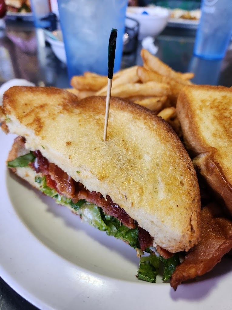 A white plate consisting of a sandwich cut in half and held together with a toothpick, served with a side of classic cut fries.