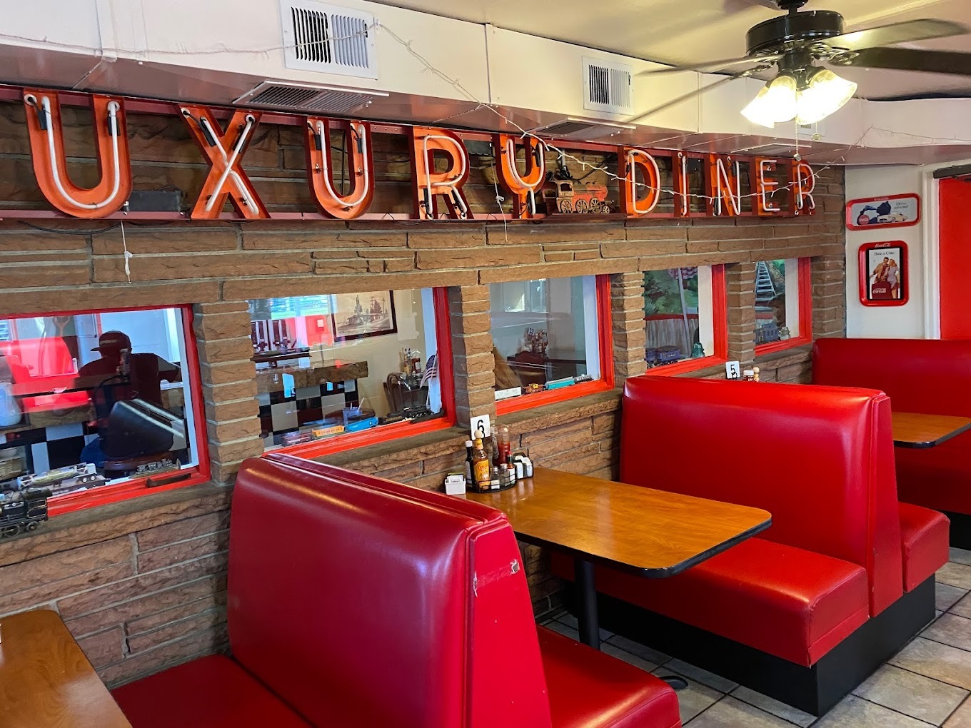 An inside view of an retro looking diner with an old lit sign above the red retro booth seating.