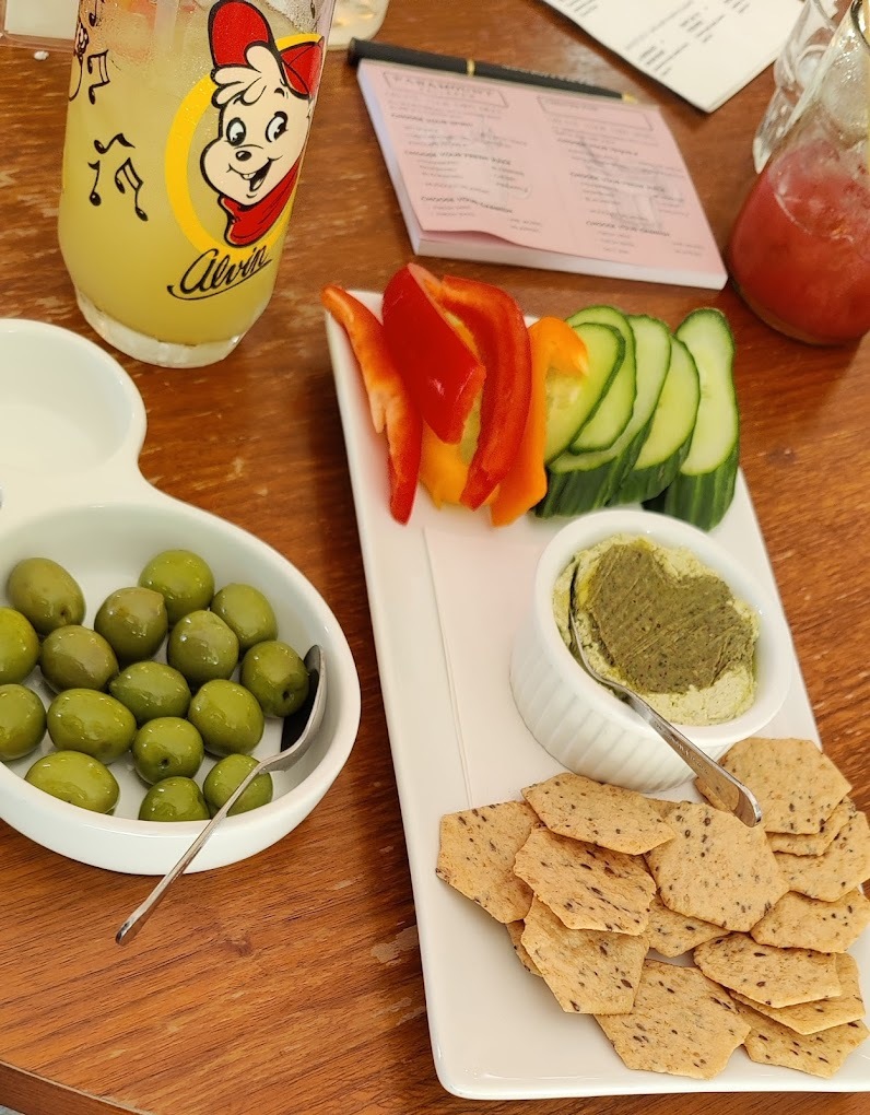 A view of a white plate with all kinds of snacking options from crackers, olives, veggies and different spreads.