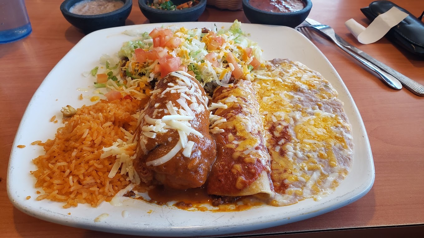 A white plate with an enchilada, rice, beans, and a side of toppings.