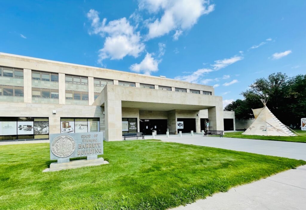 An outdoor view of a very large white concrete building with an awning above the door and a sign out front.