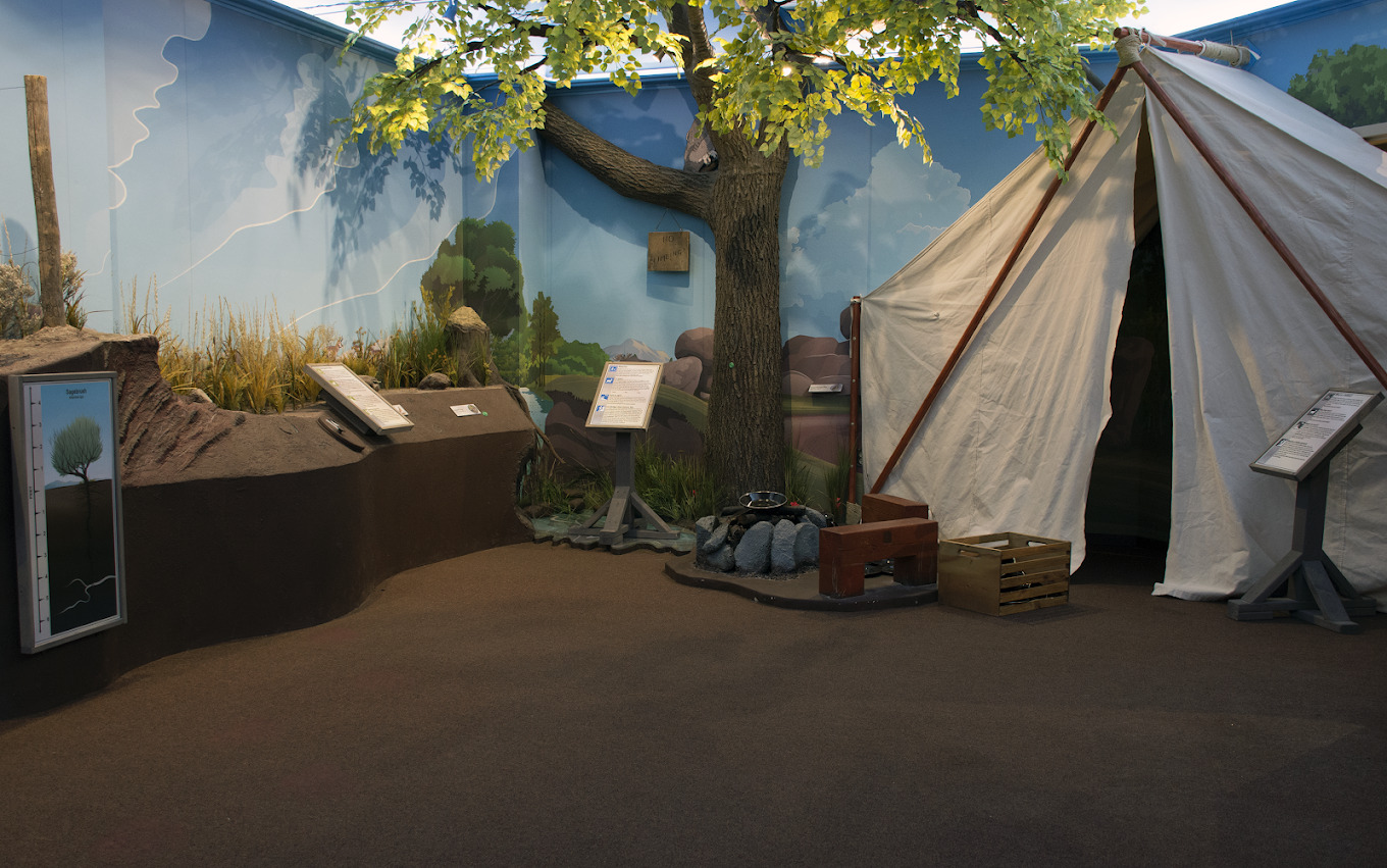 A view of a wall painted like a sky with a tent and a tree, along with pedestals to display various scripts of info.